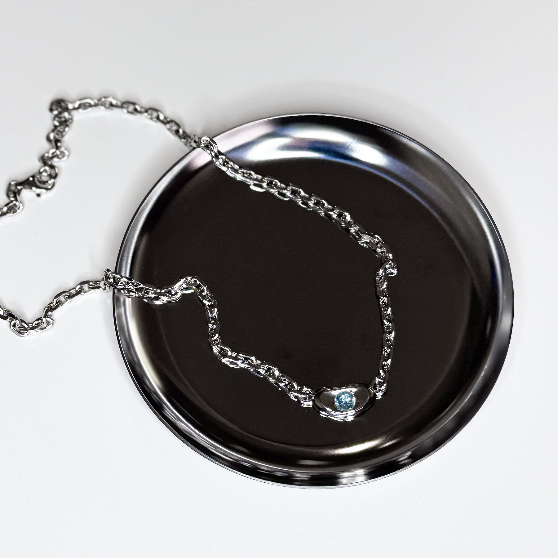 Top view of CHESI 925 sterling silver Horizon Chain with rhodium plating and sky blue topaz gemstone lying on a silver tray. 