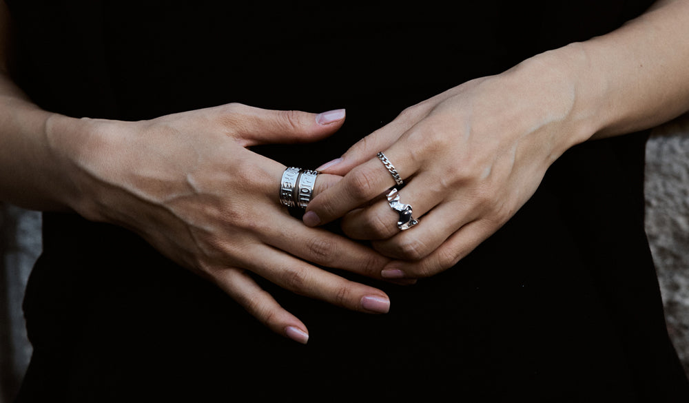 Close-up of model's hands wearing 925 sterling silver koreatown rings, abstract wrinkle ring, and thin cuban ring