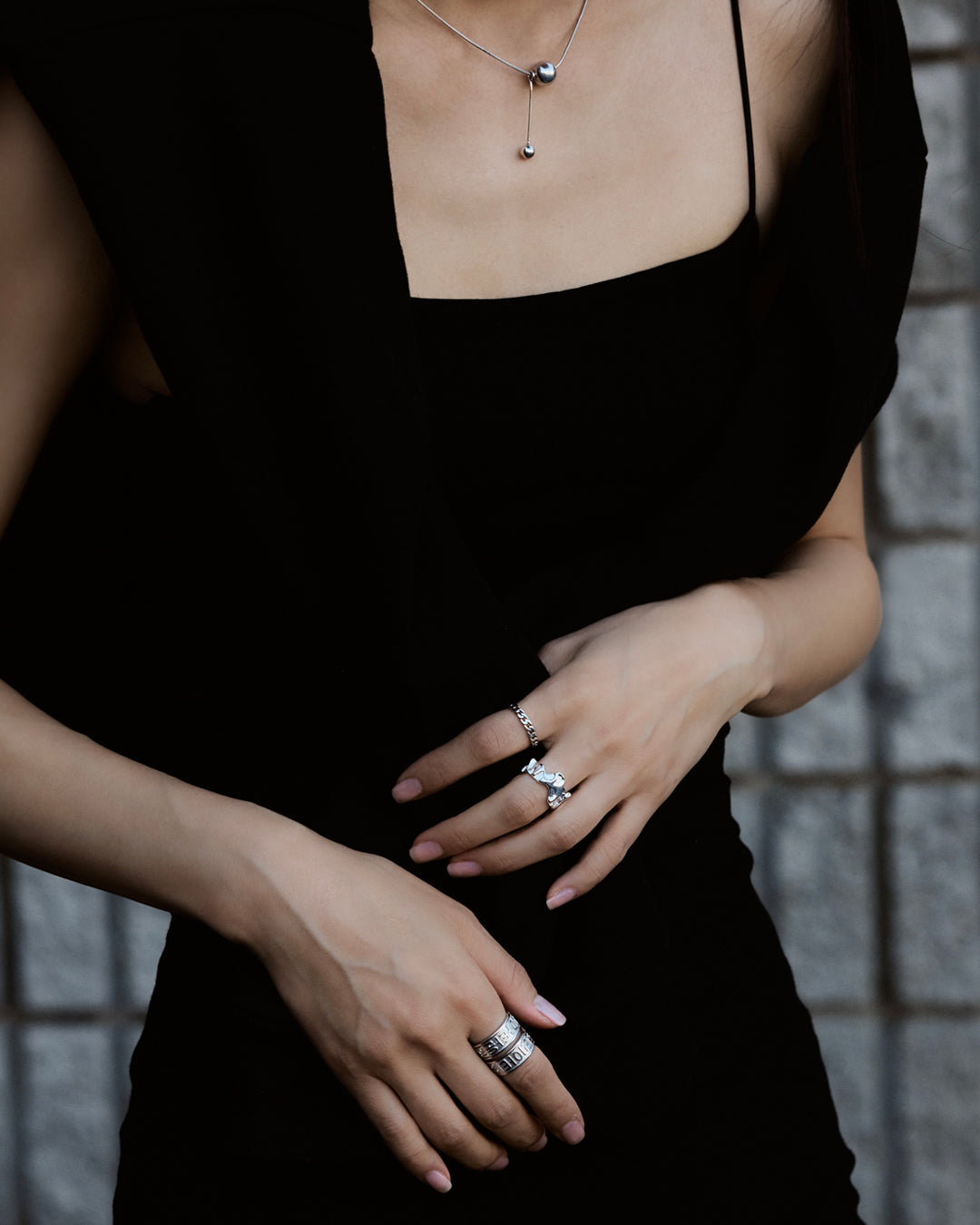Female model in black dress wearing CHESI's 925 sterling silver Orbit Charm Necklace, Koreatown Rings, Abstract Wrinkle Ring, and Thin Cuban Ring.