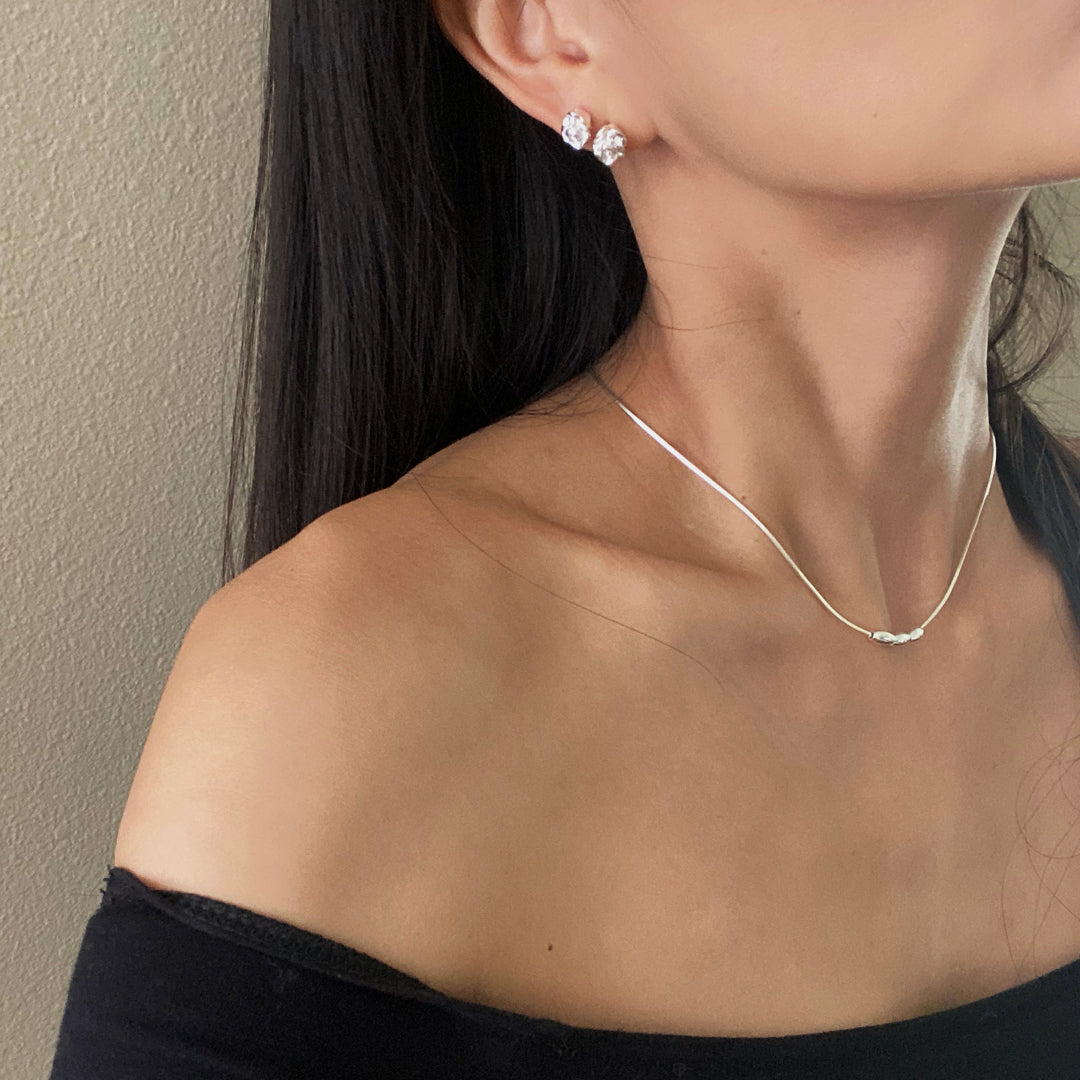 Model wearing two rosy studs on one ear with a silver triple charm necklace